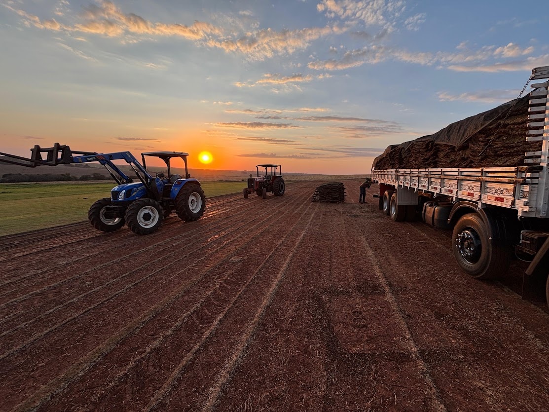 Caminhão carregado e tratores no campo ao pôr do sol, registro de produção e carregamento fornecido pela Grameira Maripá.
